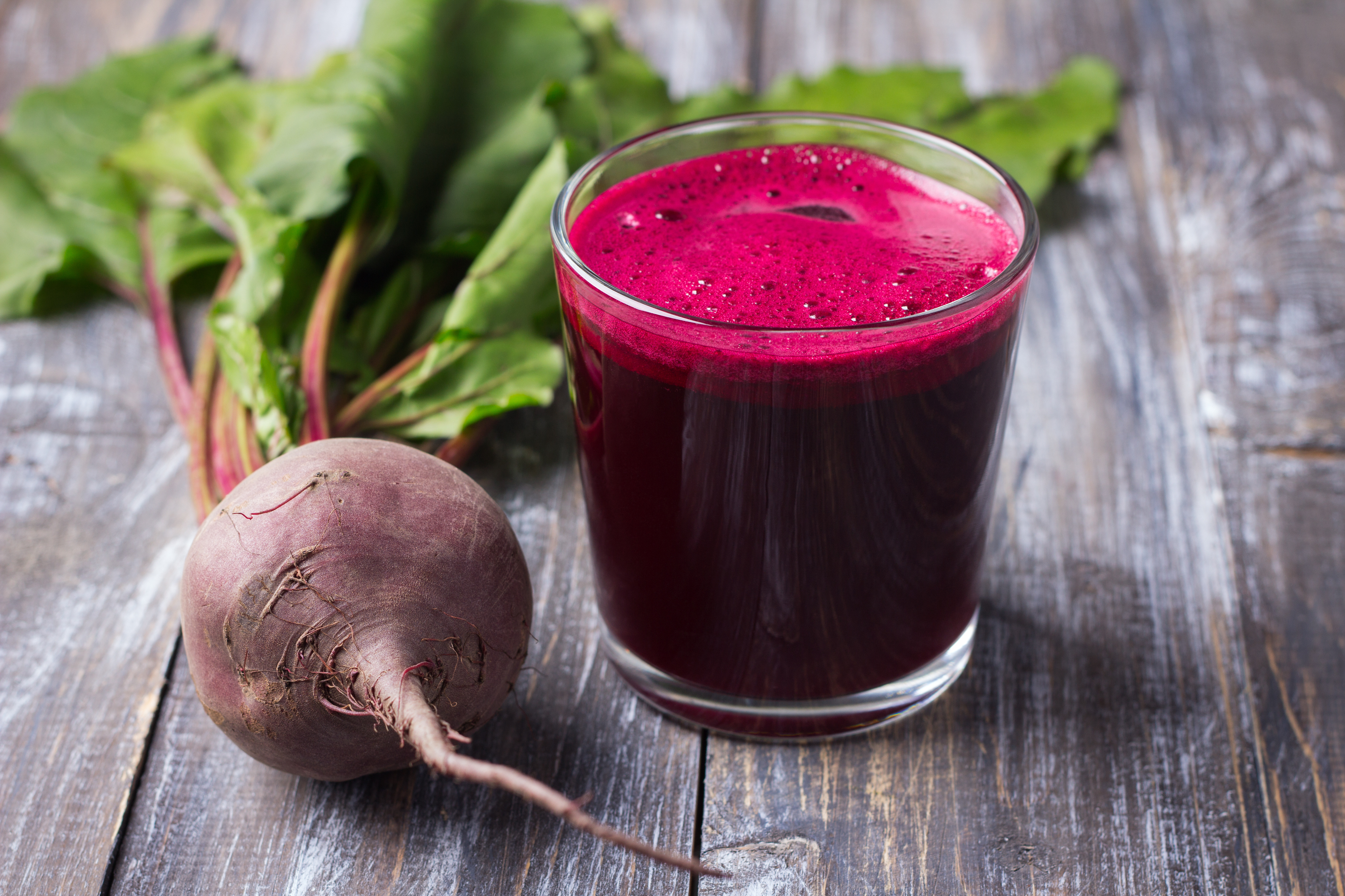 A cup of red beet juice with a beet laying on the wooden table next to it